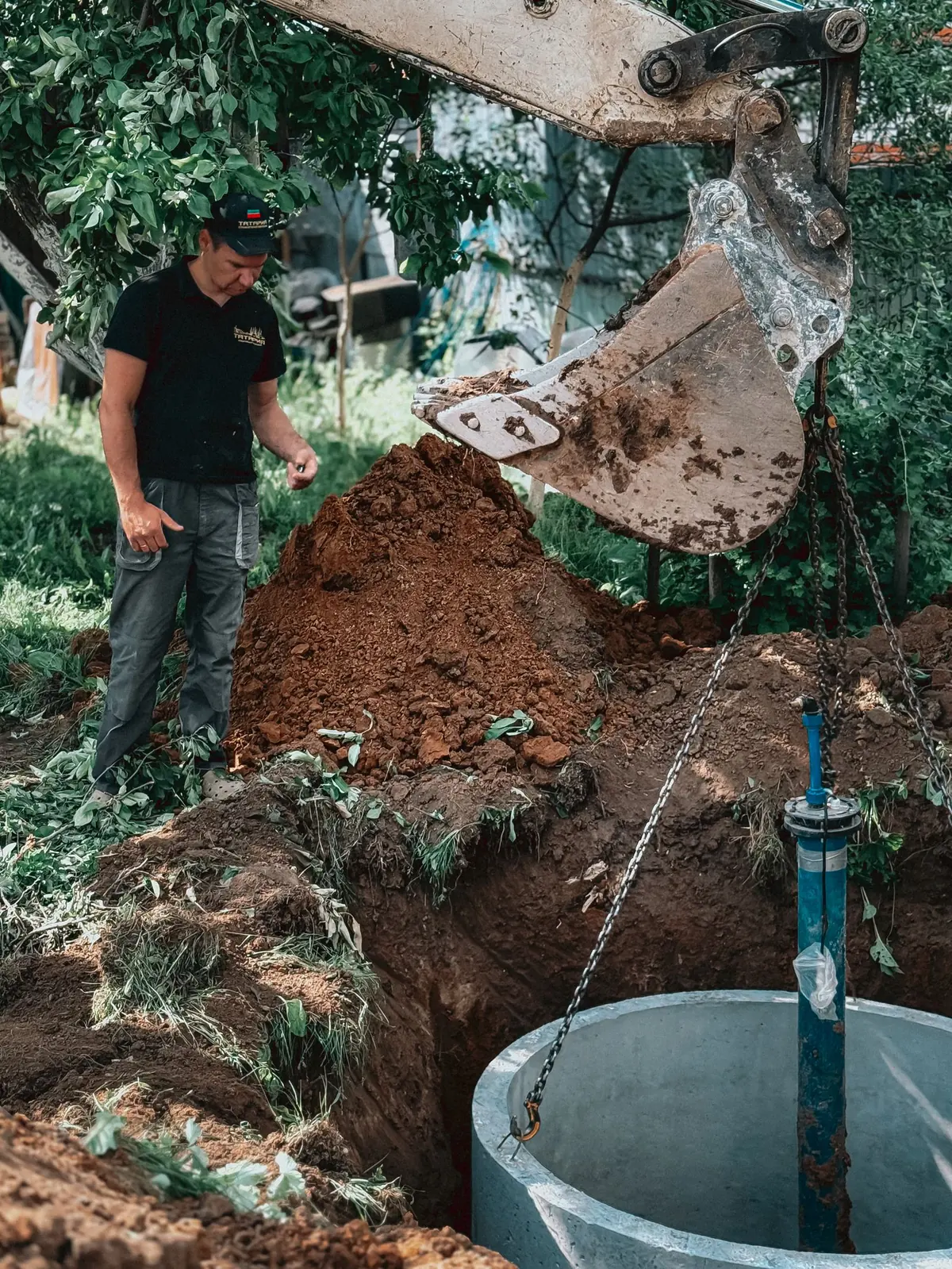 Concrete tank being lowered into an excavated pit by an excavator